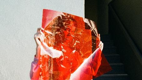 volto di donna dietro ad un foglio trasparente rosso - foto thought per unsplash.com